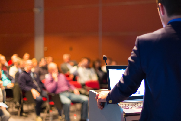 A speaker presenting at the IFE Fire Safety Conference 2024, held at the Carlton Hotel Dublin Airport. The audience is seated and attentive, with a focus on fire safety training and consultancy services.